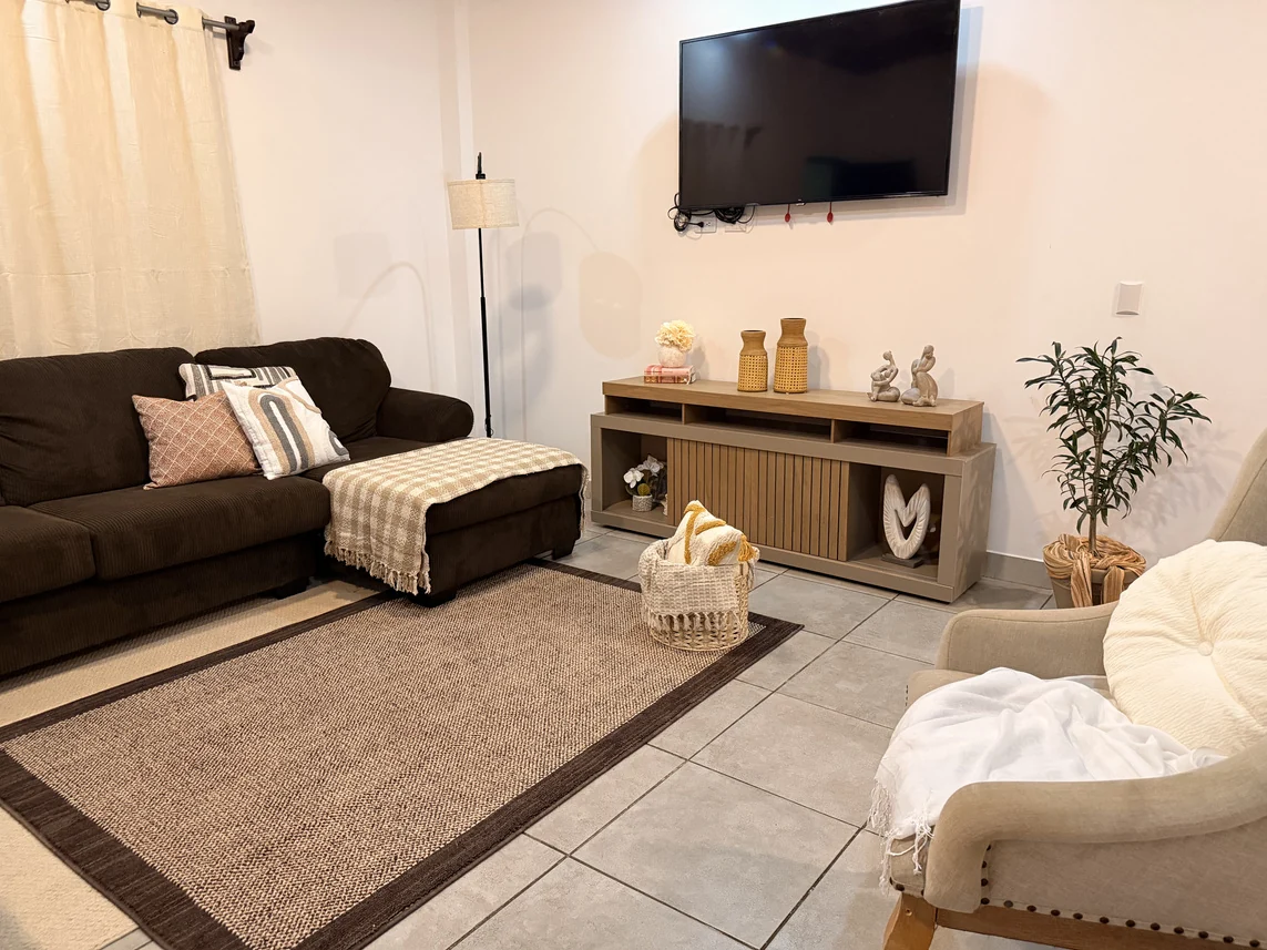 Sala con sofá marrón, consola de madera, alfombra y textiles en tonos neutros